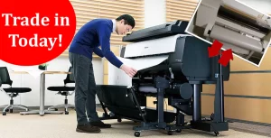 A man leans into a new large format printer while an old is in the corner, with the words trade in today!